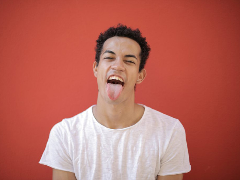 Man sticking his tongue out against a red background. Learn about the nuances of oral thrush.