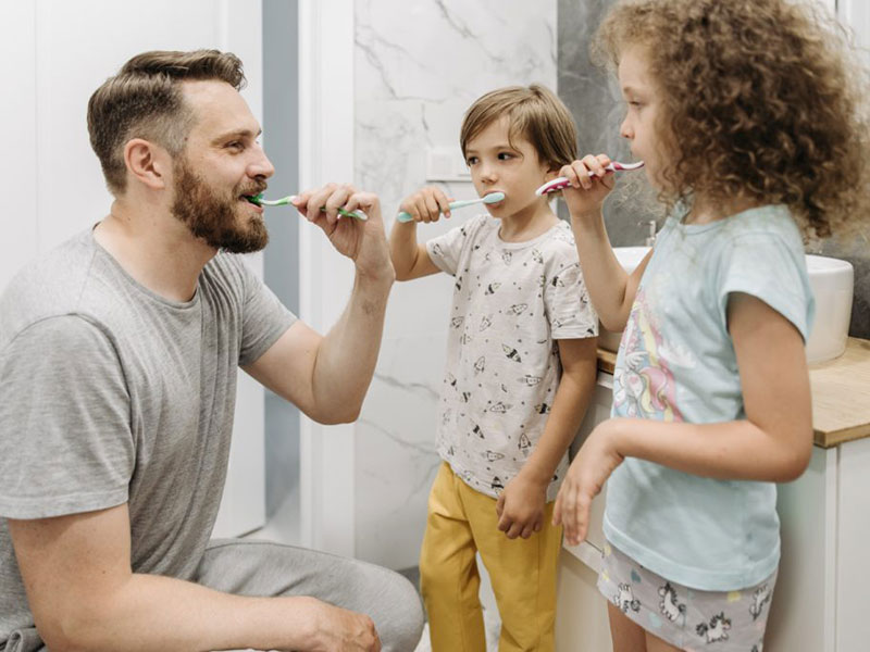 Dad brushing his teeth with two children.