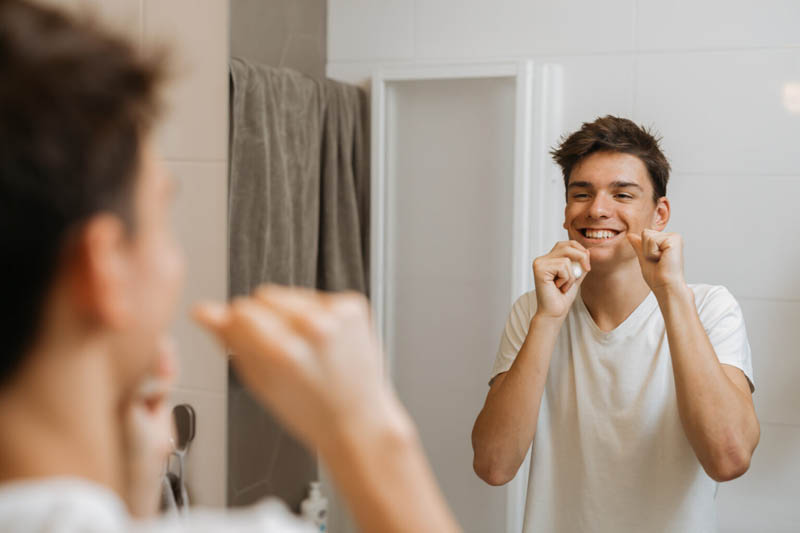 teenager boy cleaning his teeth with dental floss in his bathroom