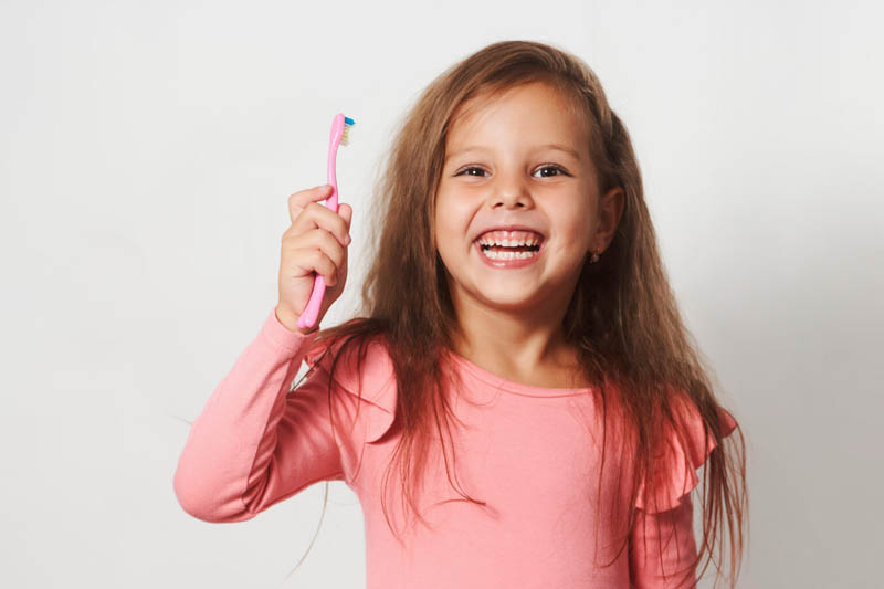 Little child girl brushing her teeth on white background.