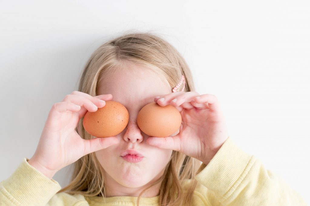 small girl holding two eggs on eyes