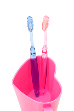 Two colorful toothbrushes are placed in a pink cup
