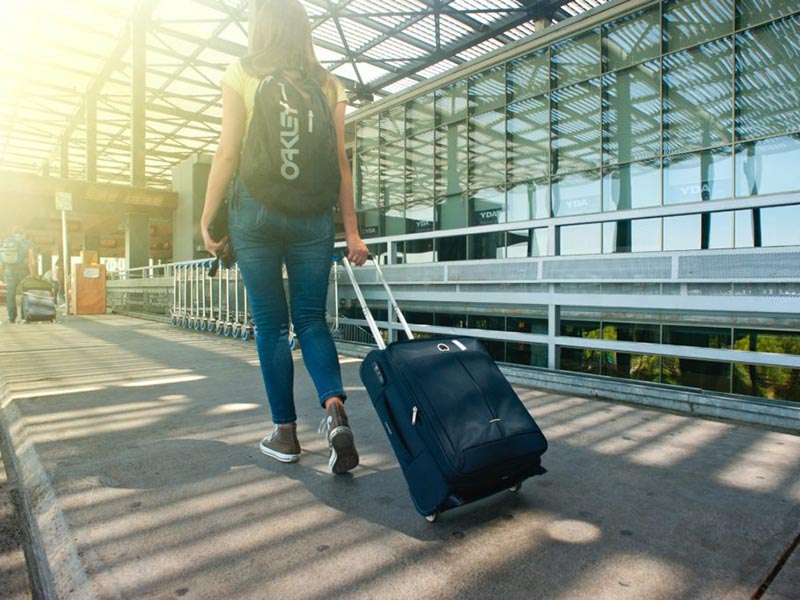 Woman walking through an airport with rolling luggage.