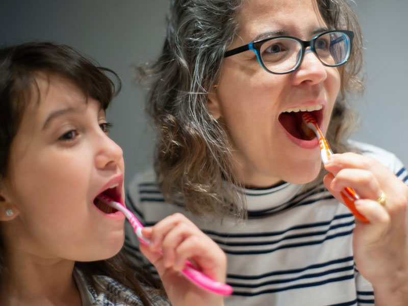 A mother and daughter brushing their teeth together.