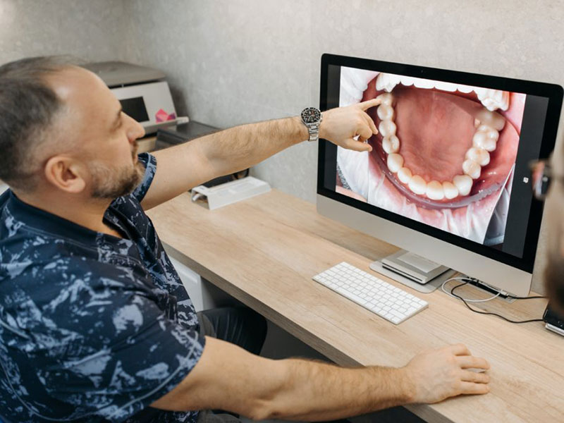 A dentist showing a patient a set of teeth displayed on a computer.