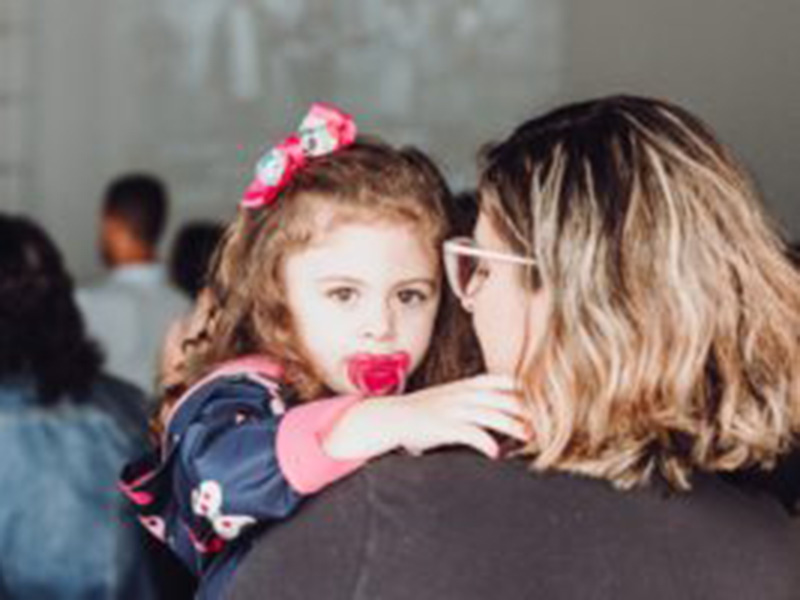 Toddler with a pacifier in her mouth being held by an adult.