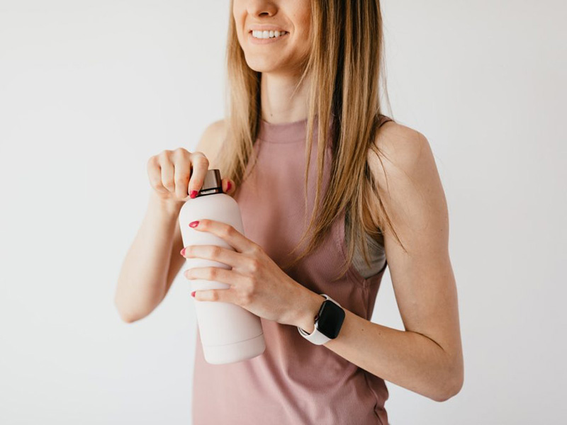 woman holding water bottle and smiling with white teeth.